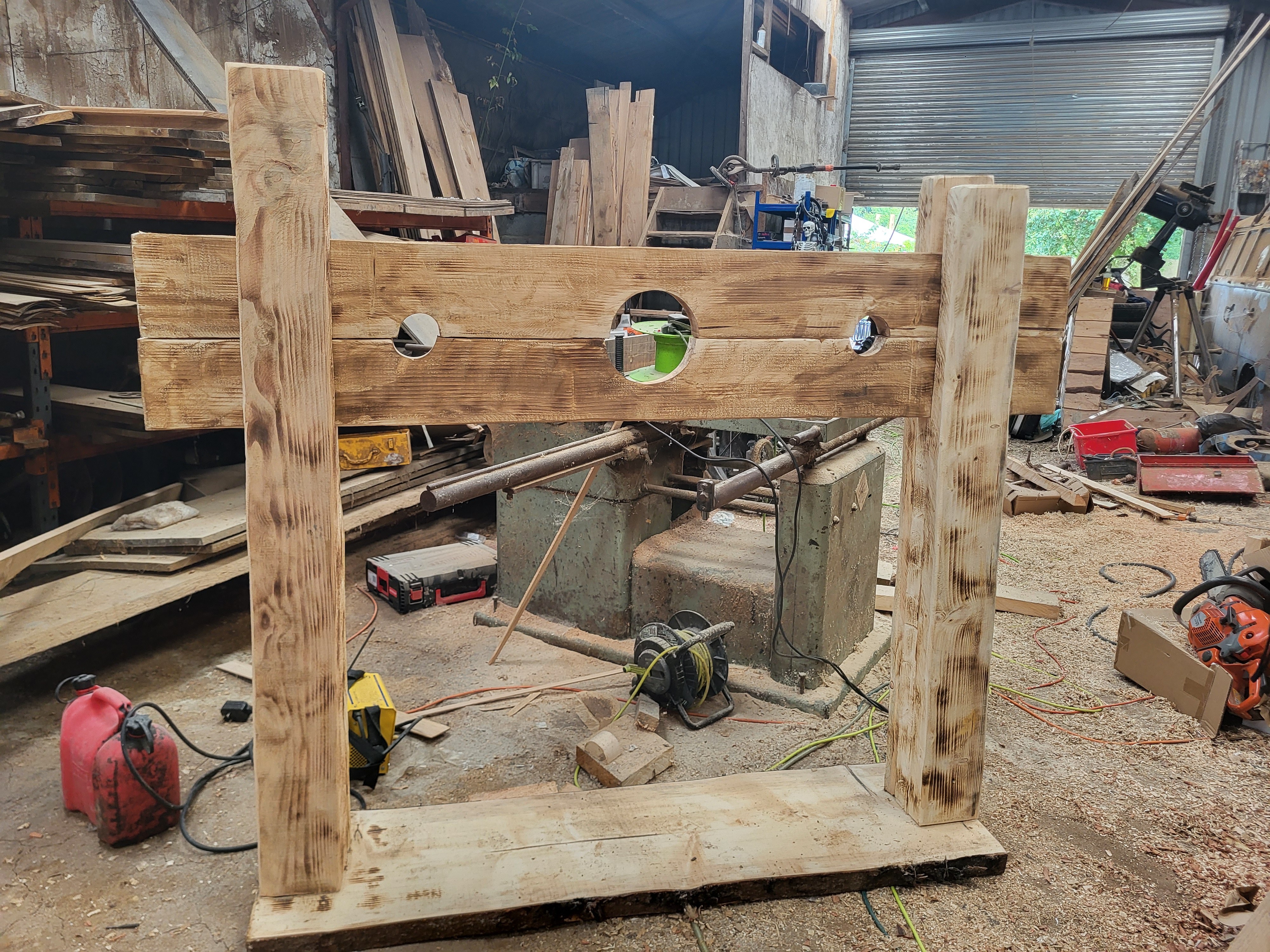 Wooden stocks used for restraint with three circular holes in a workshop filled with tools.