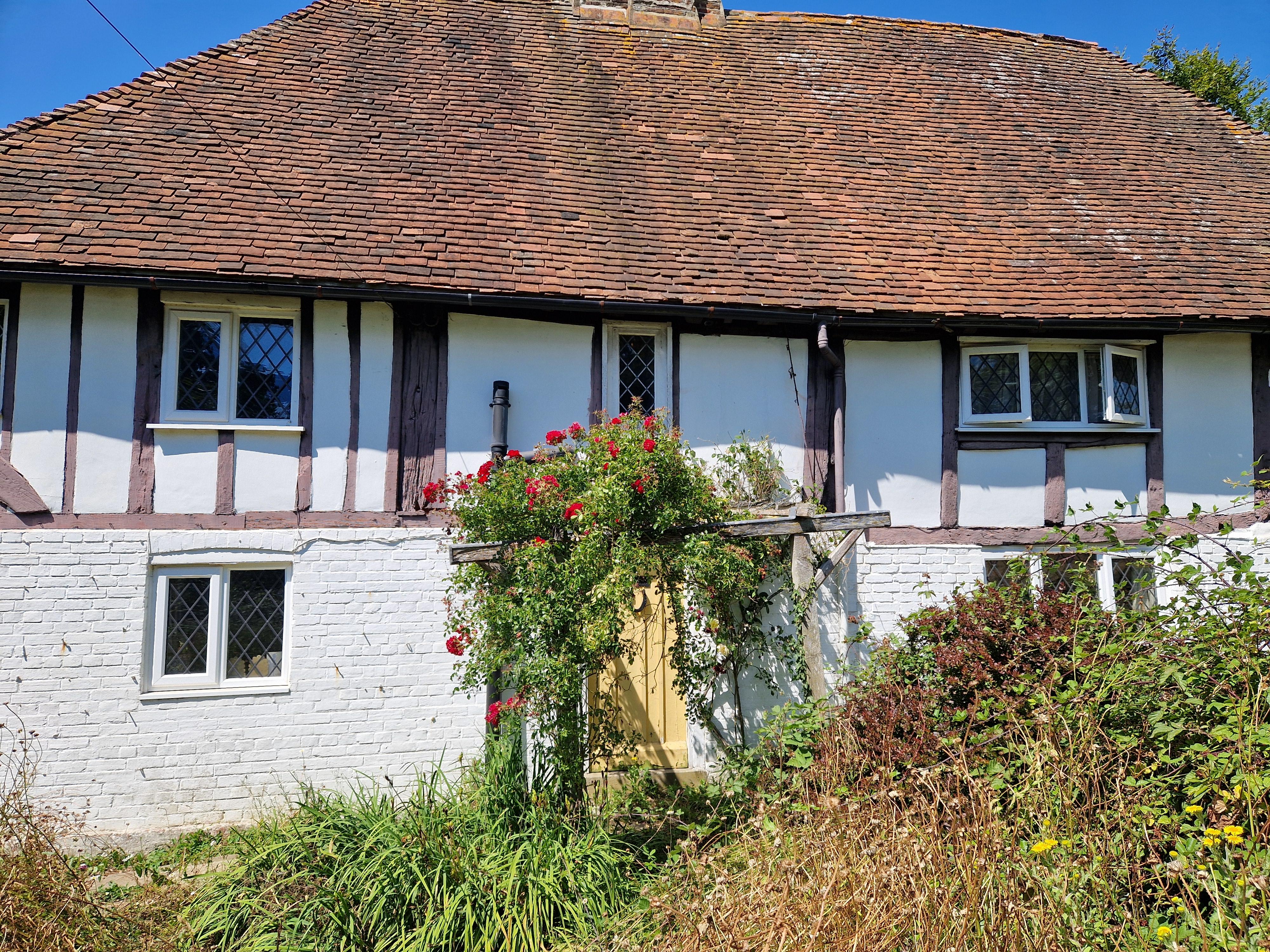 Cottage with white brick lower walls, timber upper walls, a red tiled roof, and a door with flowering vines.
