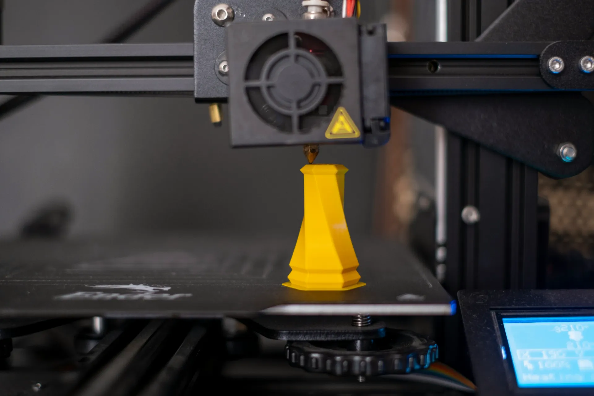 3D printer nozzle printing a yellow chess rook figure on the printer bed.