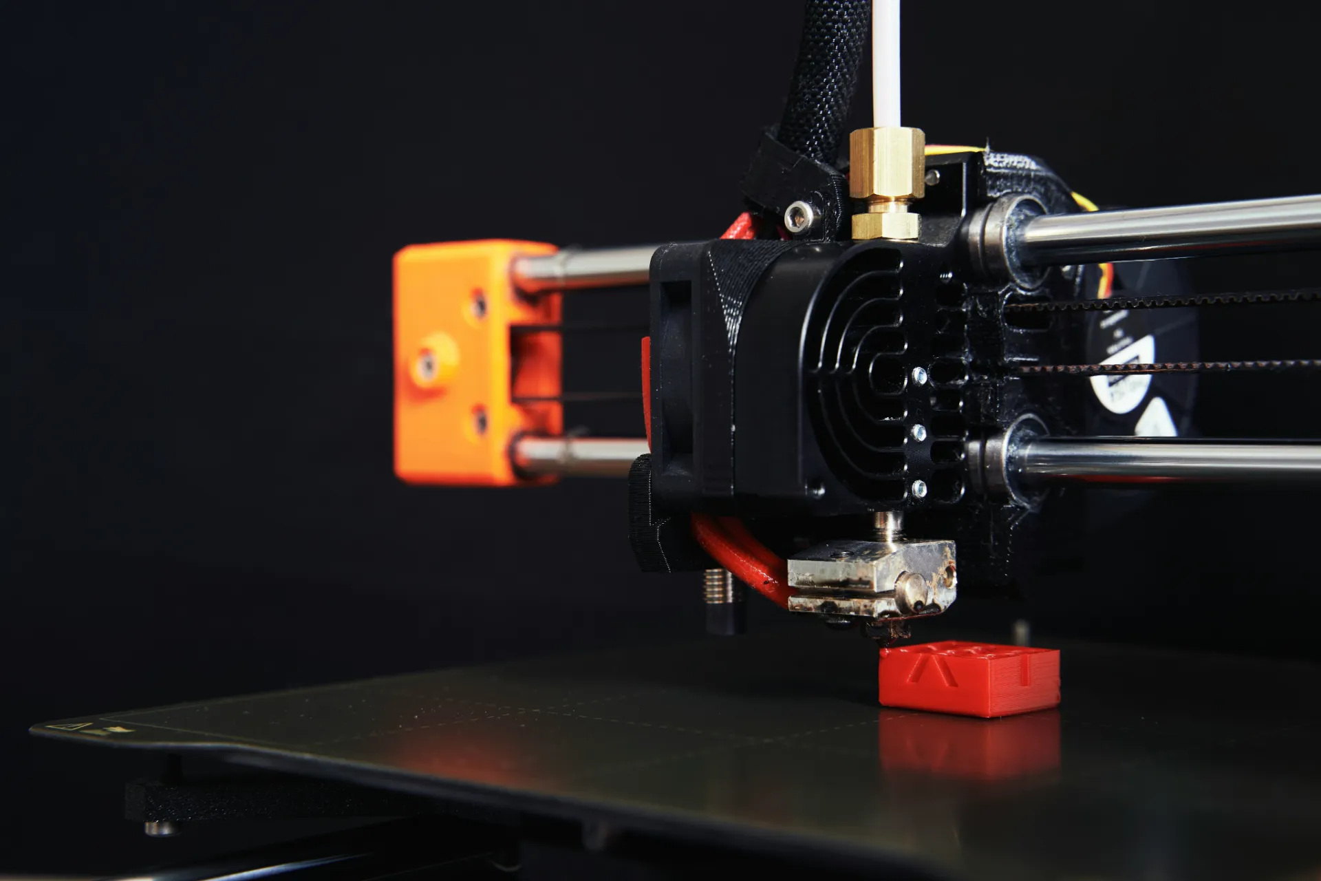 Close-up of a 3D printer nozzle extruding red plastic to create a small object on the build plate.