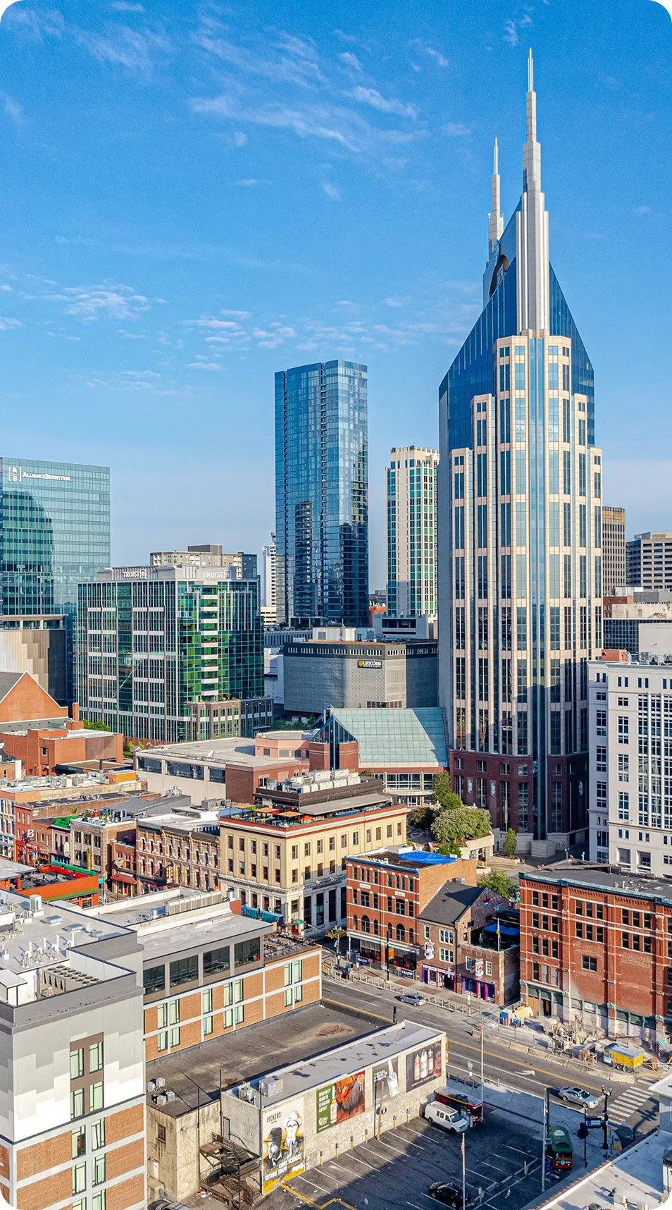 City skyline featuring a tall modern skyscraper with spires, surrounded by shorter buildings under a blue sky.