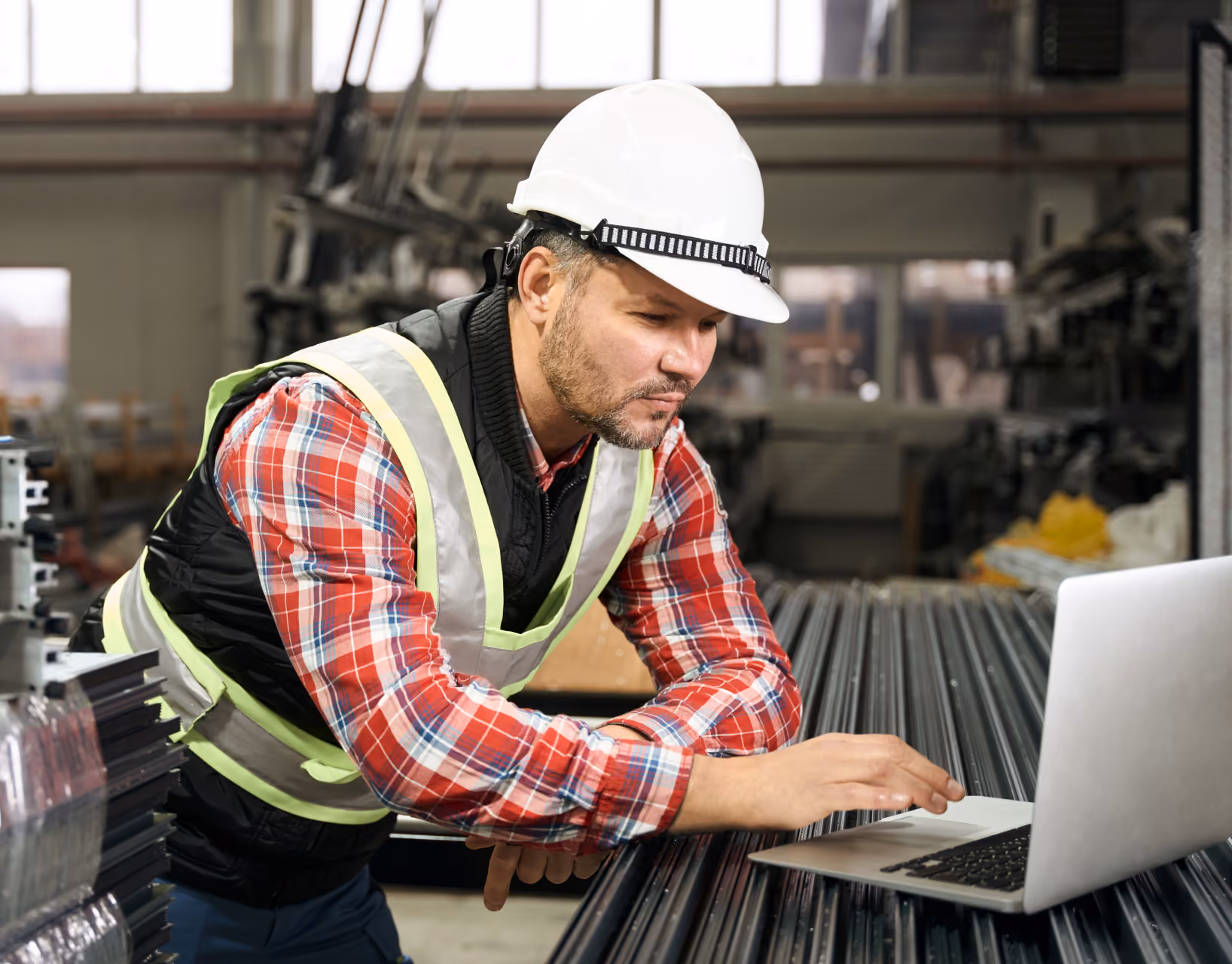 Worker in a hard hat using a laptop in a steel yard