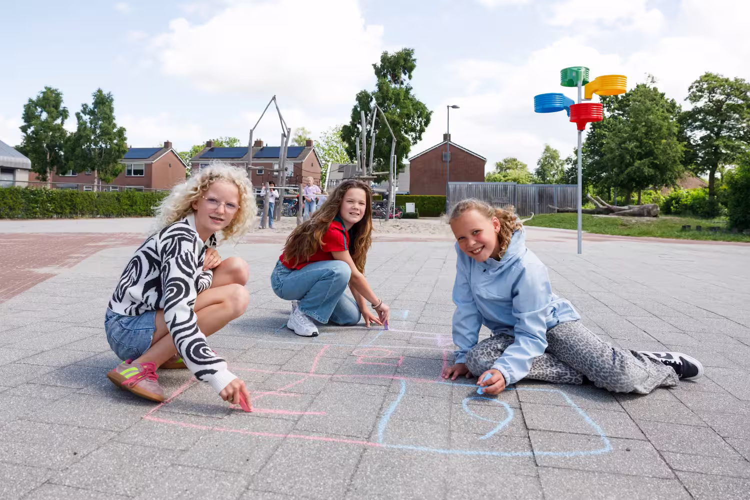 Drie meisjes tekenen samen met stoepkrijt op een plein buiten in een woonwijk.