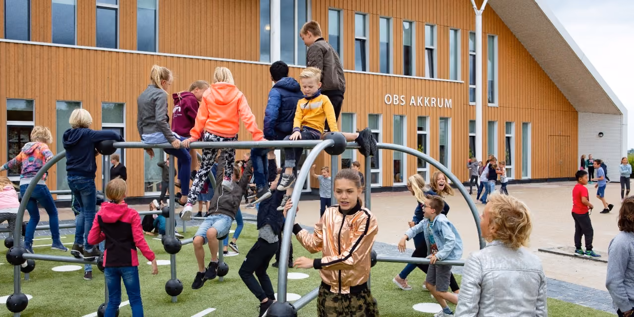Kinderen spelen op klimrek en rennen buiten schoolgebouw OBS Akkrum.