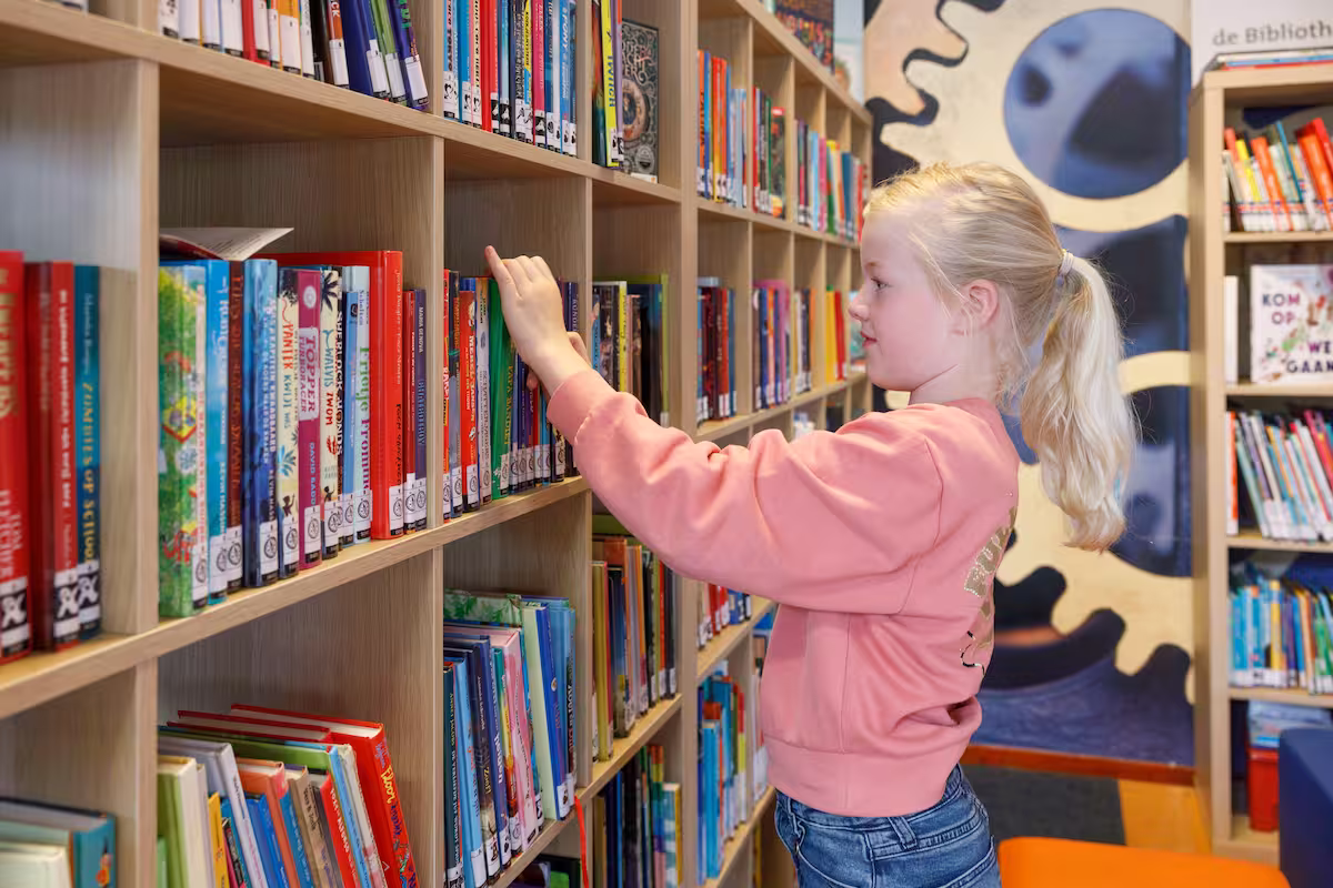 Meisje met een paardenstaart pakt een boek uit een boekenplank in de bibliotheek.