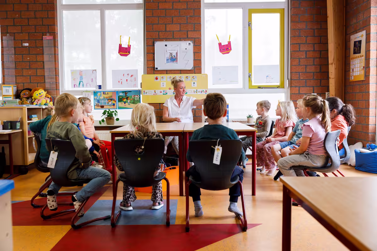 Een leraar leest aan een groep jonge kinderen die in een kring in een klaslokaal zitten.