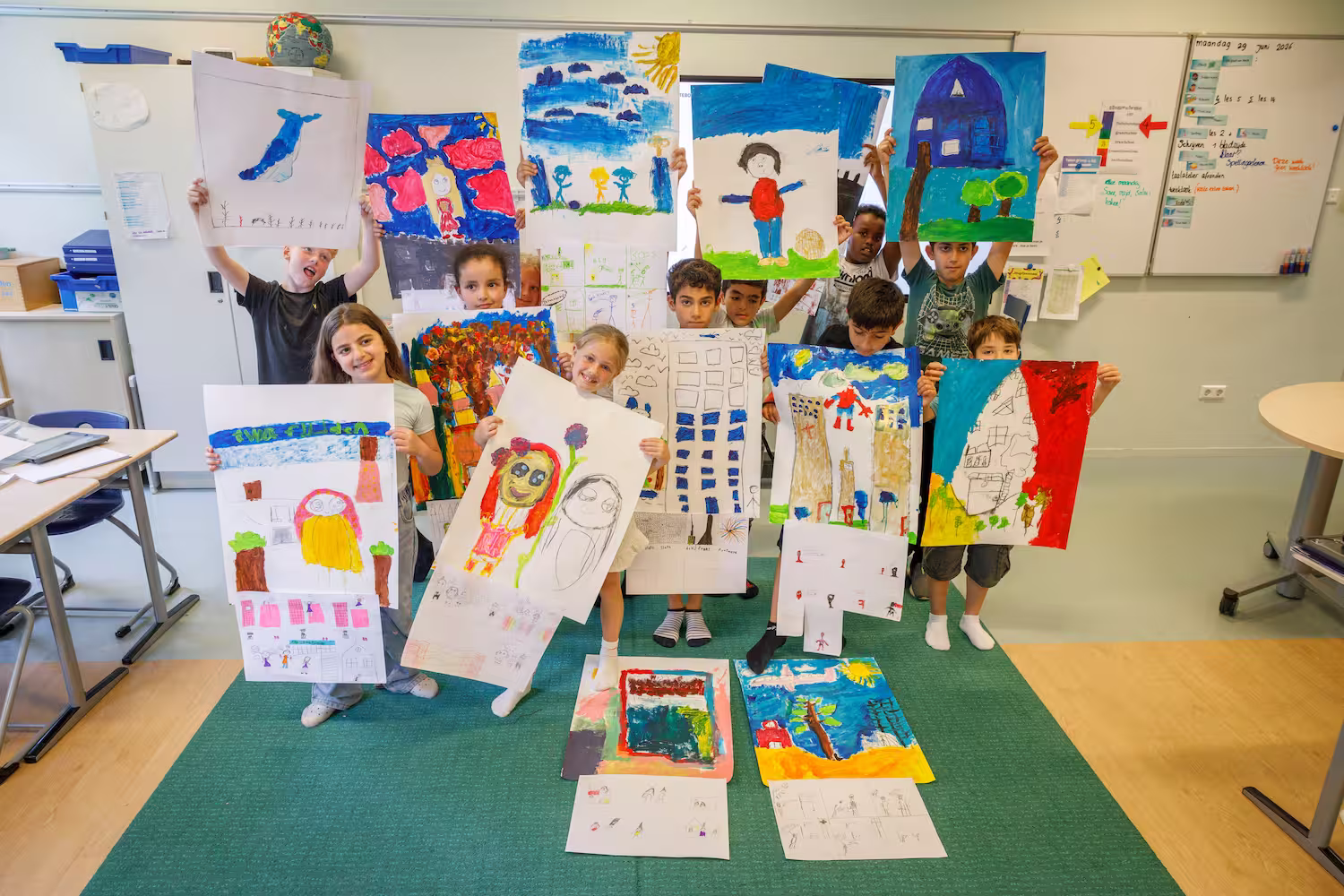 Groep kinderen in klaslokaal toont kleurrijke tekeningen en schilderijen op papier.