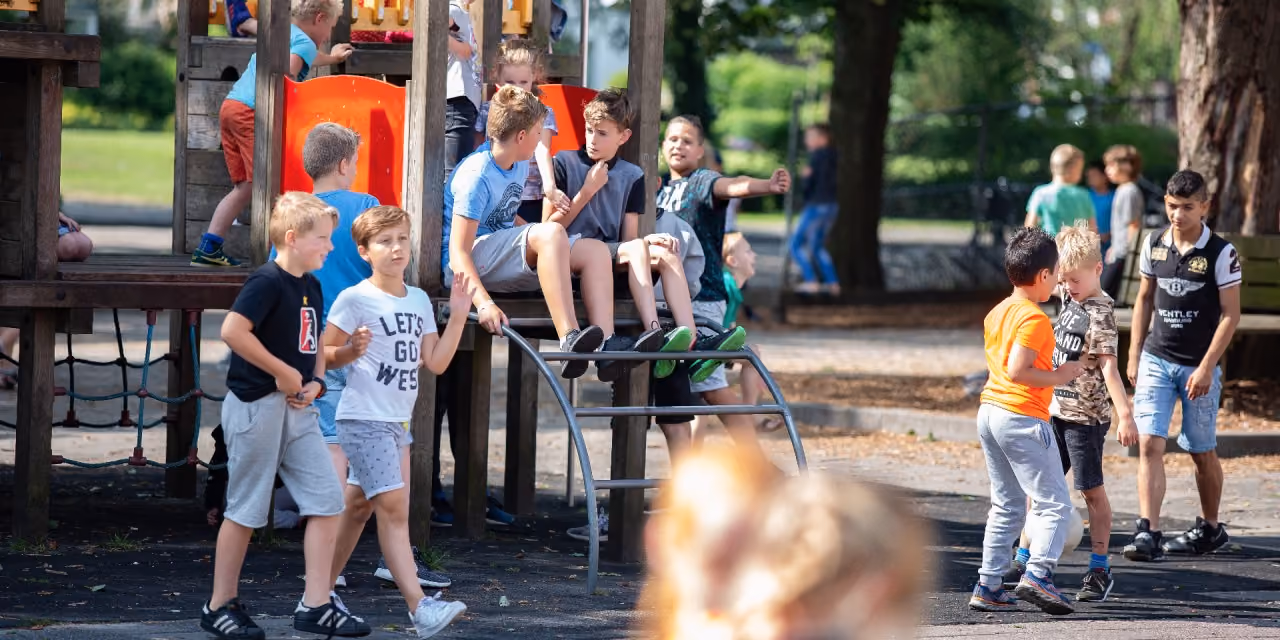 Kinderen spelen en praten samen op een speelplaats met klimrek en glijbaan buiten.
