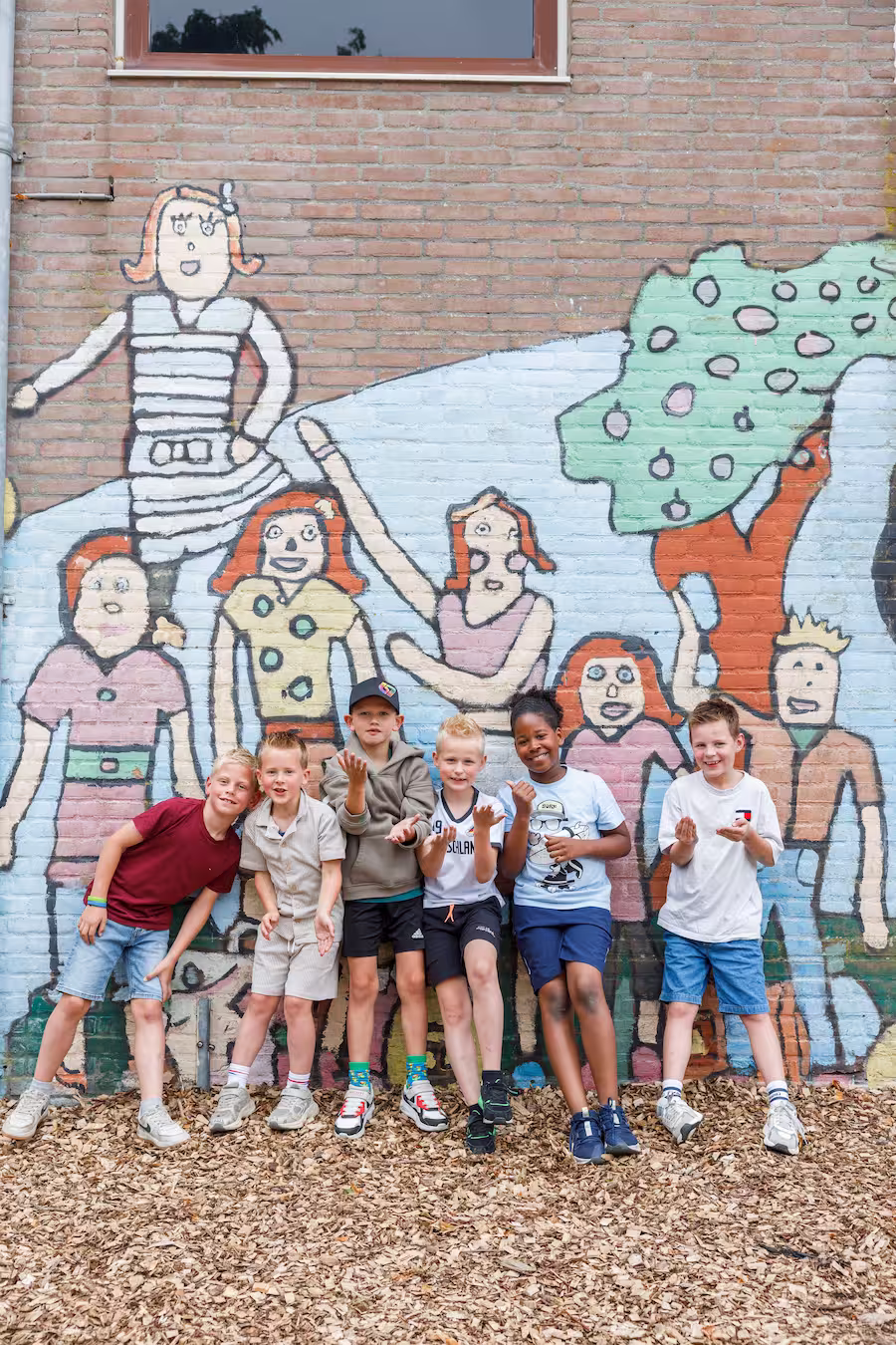 Zes lachende kinderen staan voor een kleurrijke muur met geschilderde figuren.