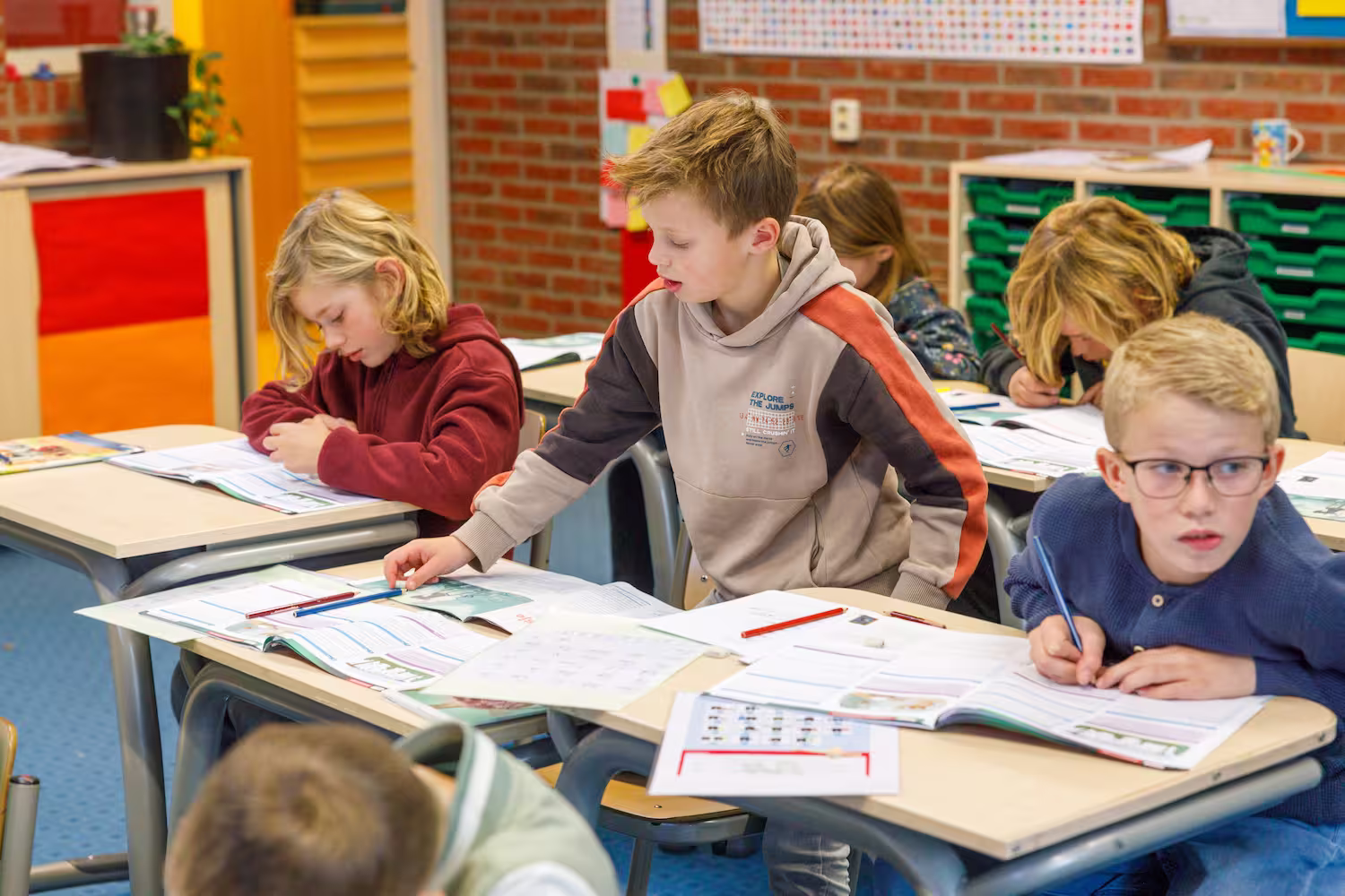 Kinderen in een klaslokaal werken geconcentreerd aan hun huiswerk aan tafels.