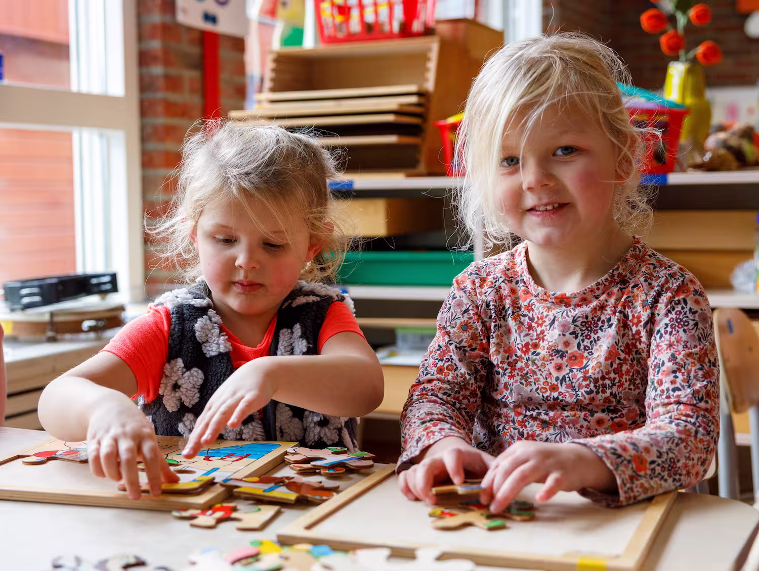 Twee jonge meisjes zitten aan een tafel en maken houten puzzels in een klaslokaal.