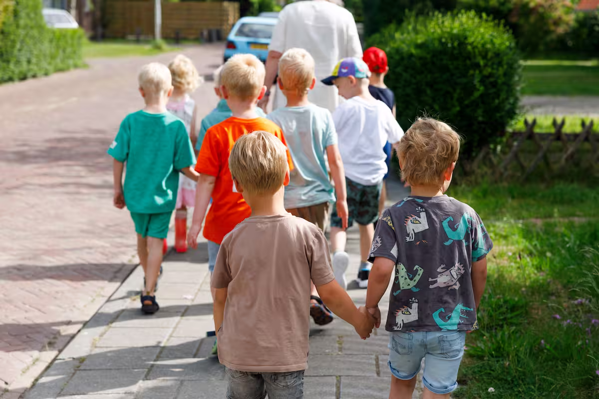 Een groep kinderen loopt buiten, twee jongens houden elkaars handen vast.