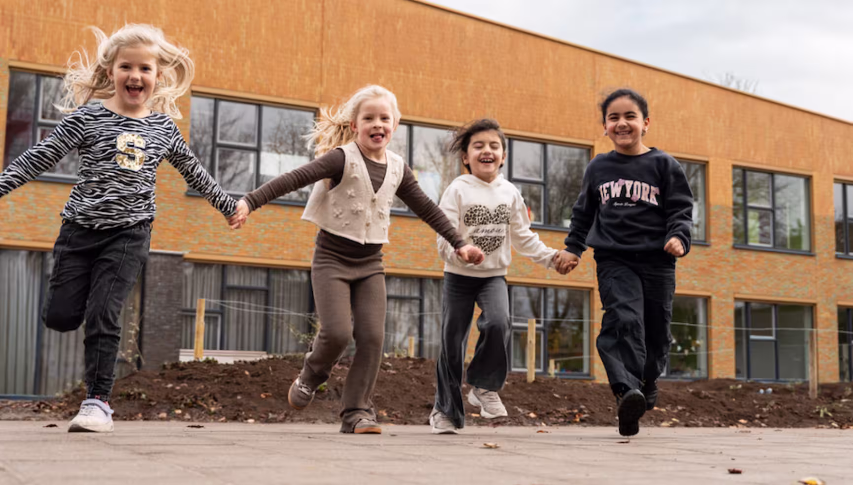 Vier kinderen houden elkaars handen vast en rennen met een gebouw op de achtergrond.