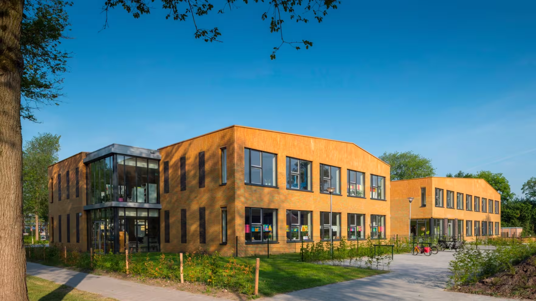 Moderne tweeverdiepingen schoolgebouw met gele bakstenen en grote ramen bij zonnige blauwe lucht.