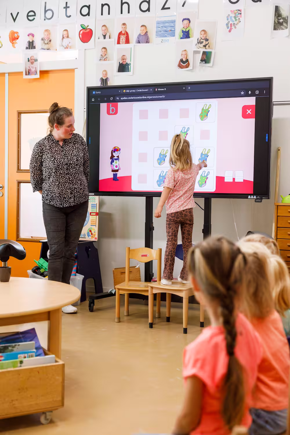Klaslokaal met een lerares, kind dat een spel op een groot scherm speelt en kinderen die toekijken.