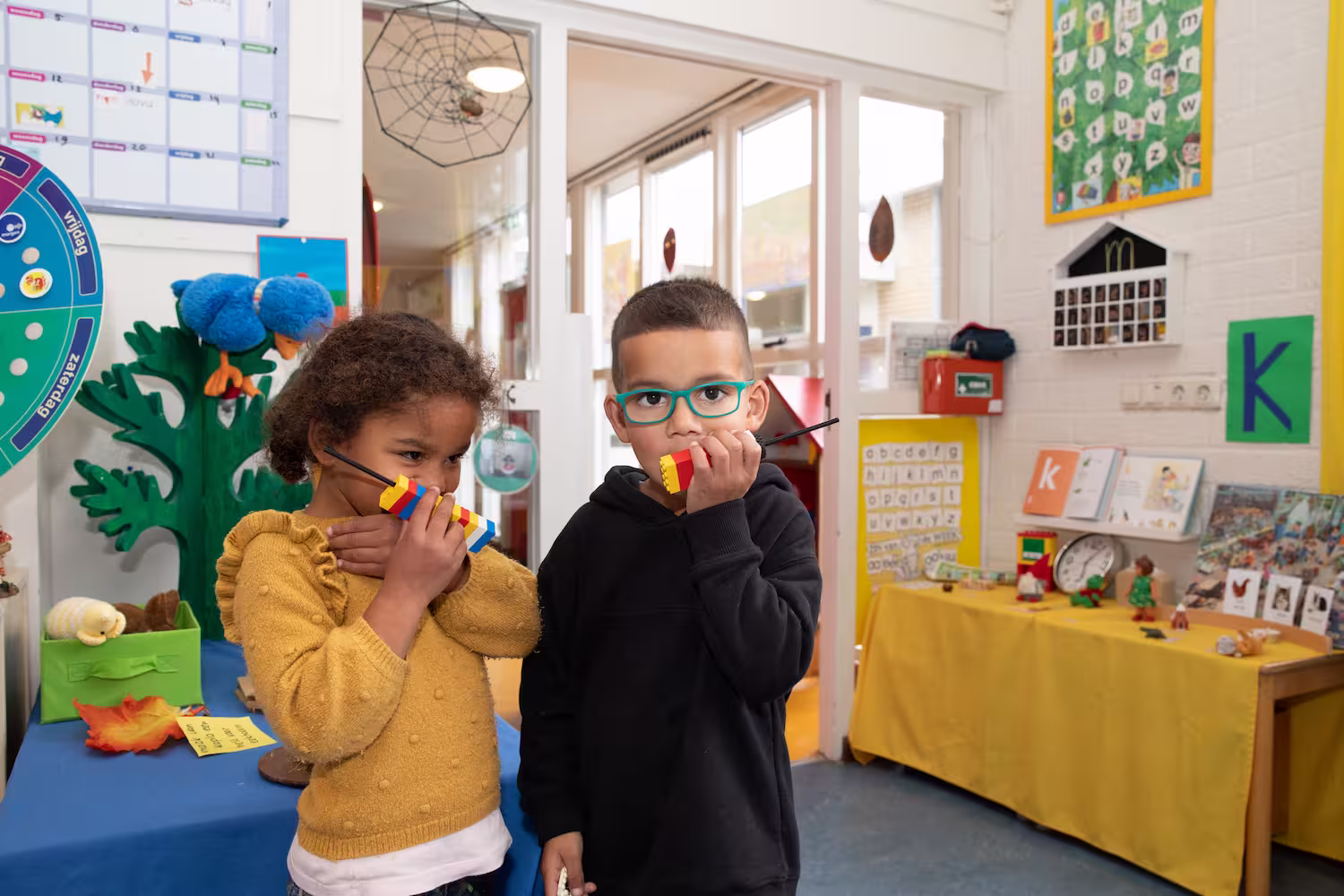 Twee kinderen in een klaslokaal die met blokken als walkietalkies spelen.