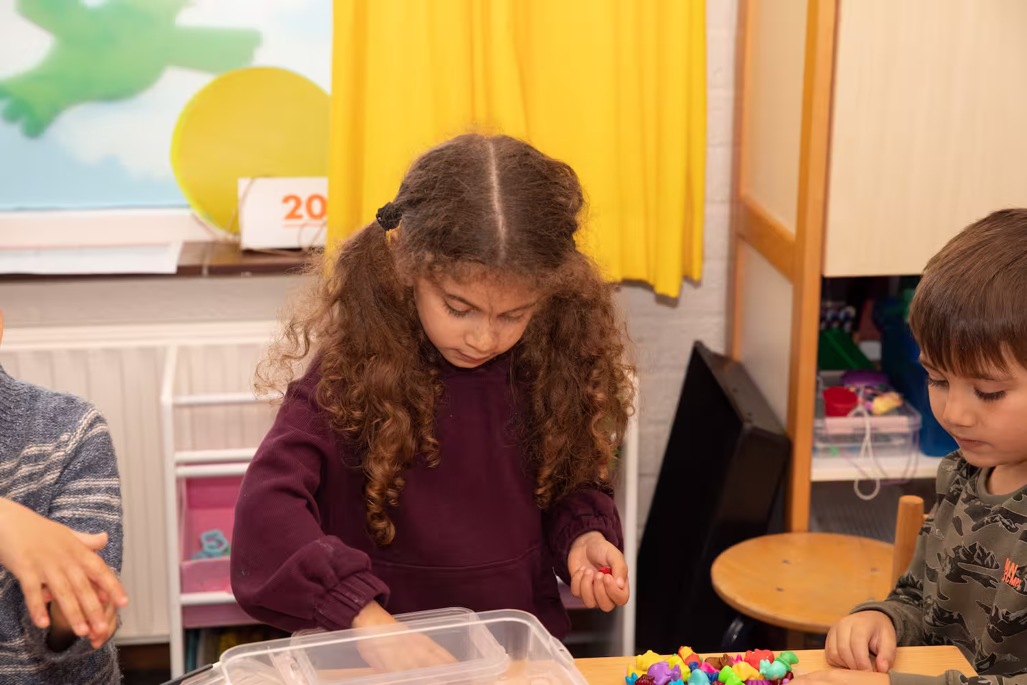 Twee kinderen spelen met kleurrijke plastic figuren aan een houten tafel in een klaslokaal.