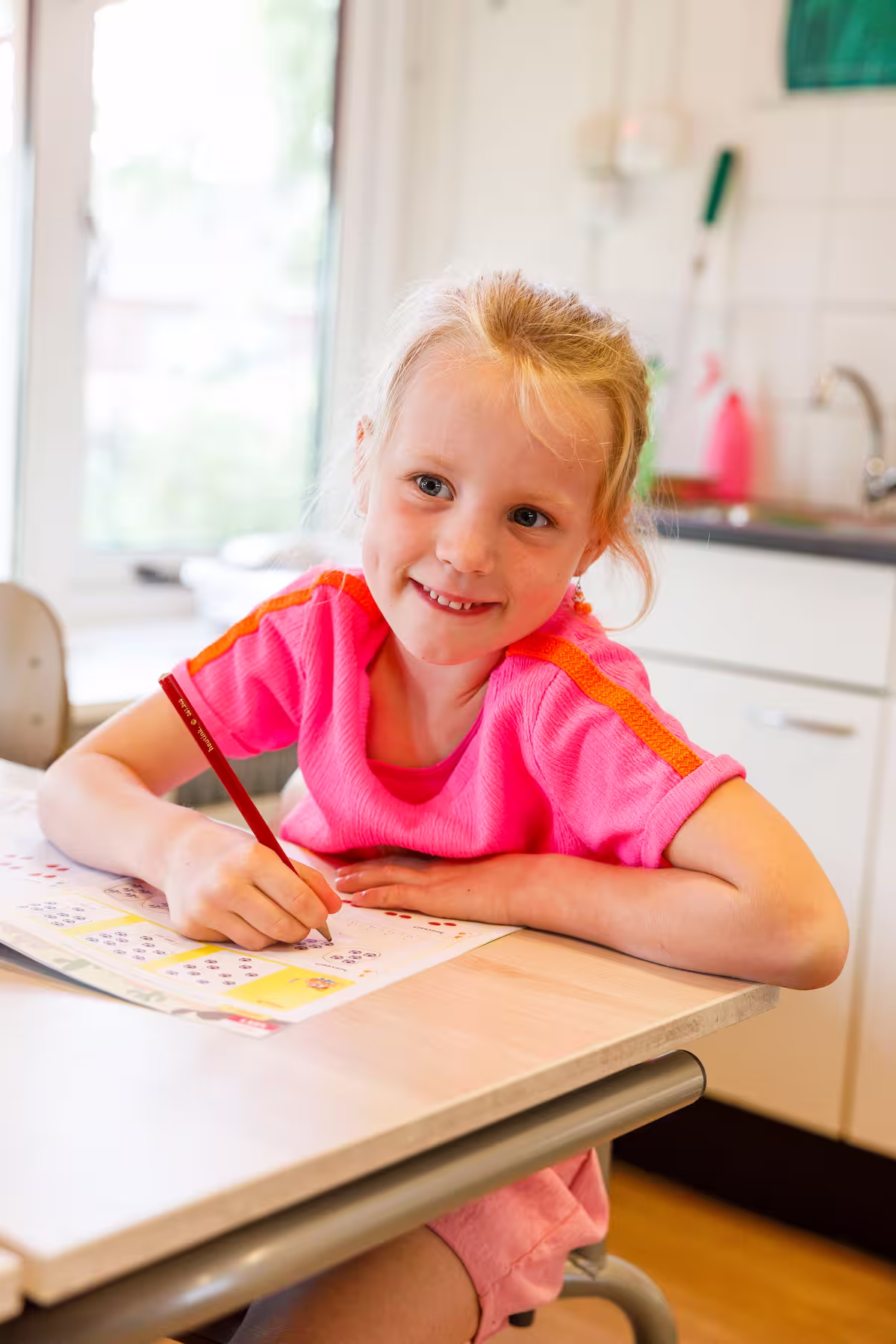 Meisje in een roze shirt dat aan tafel zit en met een potlood werkt aan een werkblad.