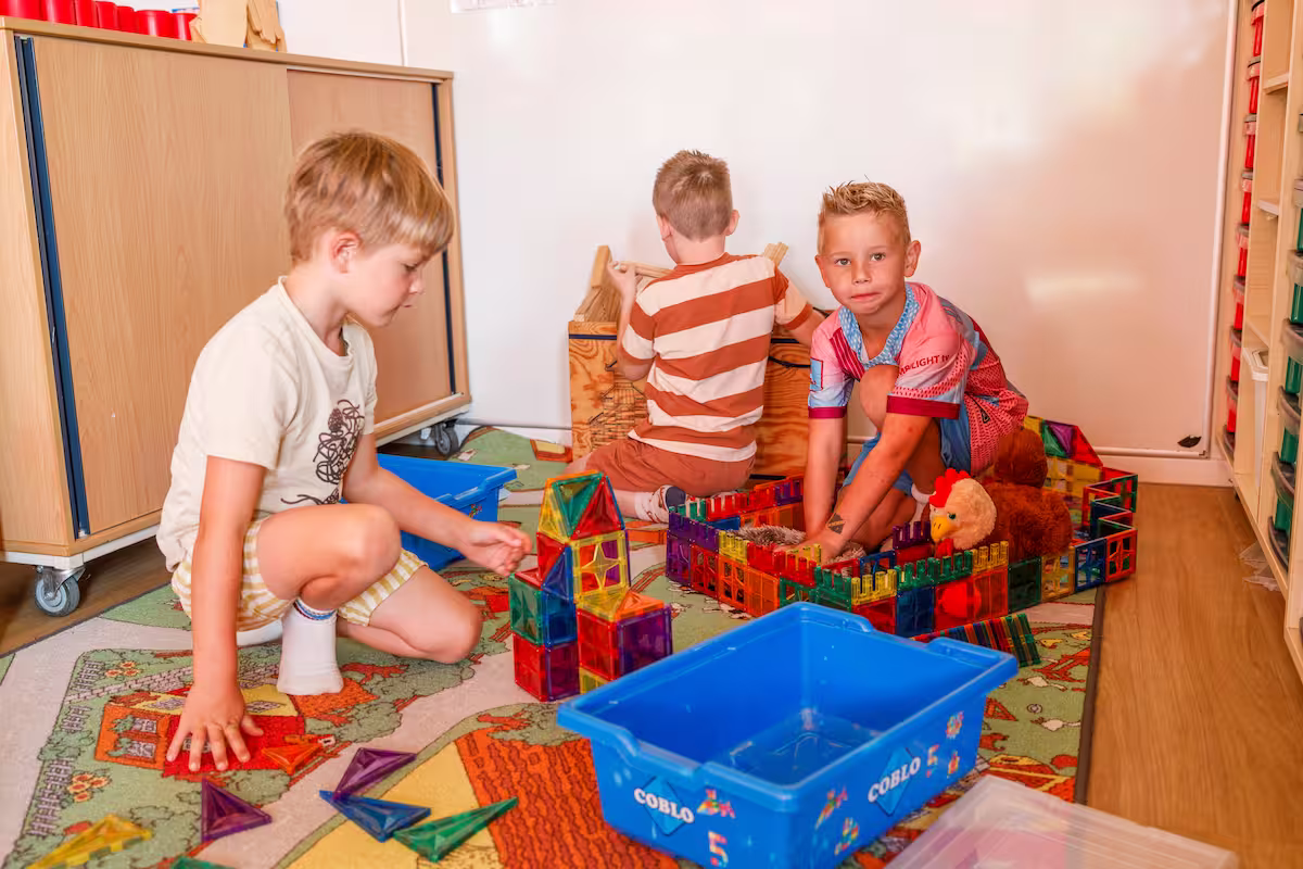 Drie jonge jongens spelen op de vloer met gekleurde magnetische bouwstenen in een klaslokaal.