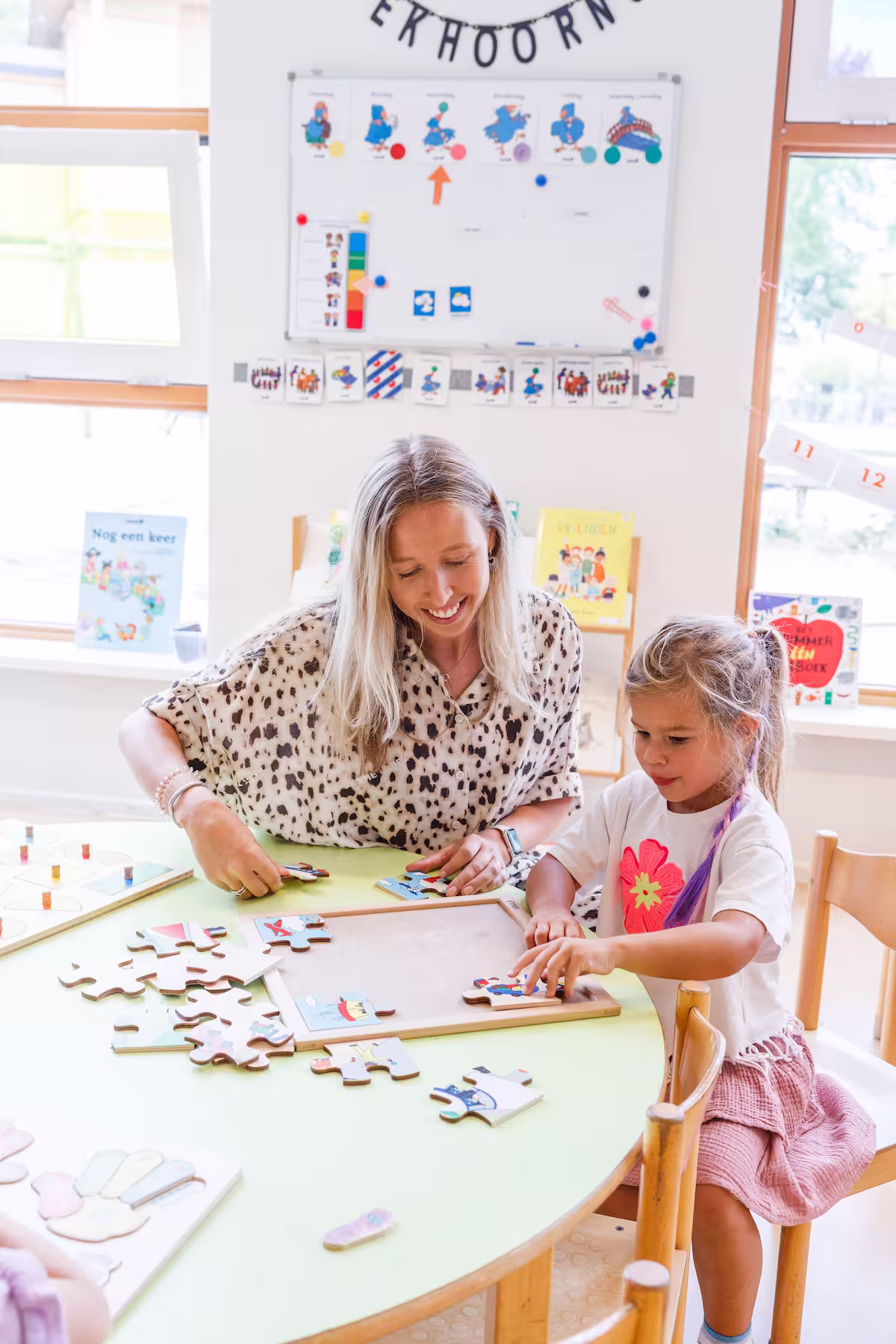 Vrouw en meisje maken samen een puzzel aan een tafel in een lichte klaslokaalomgeving.