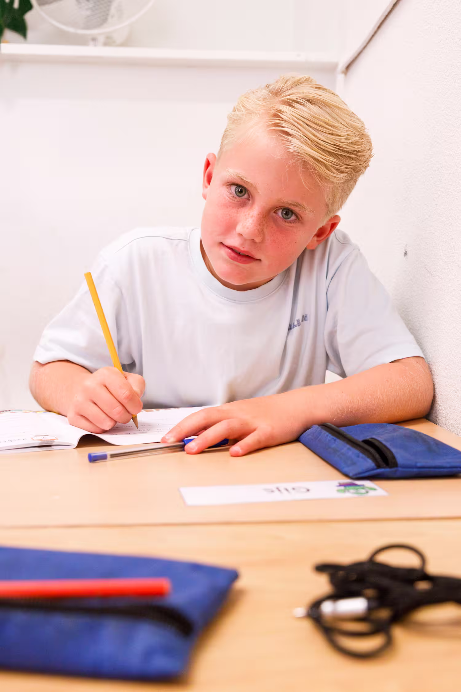 Jongen met blond haar schrijft met potlood aan een bureau tijdens het maken van huiswerk.