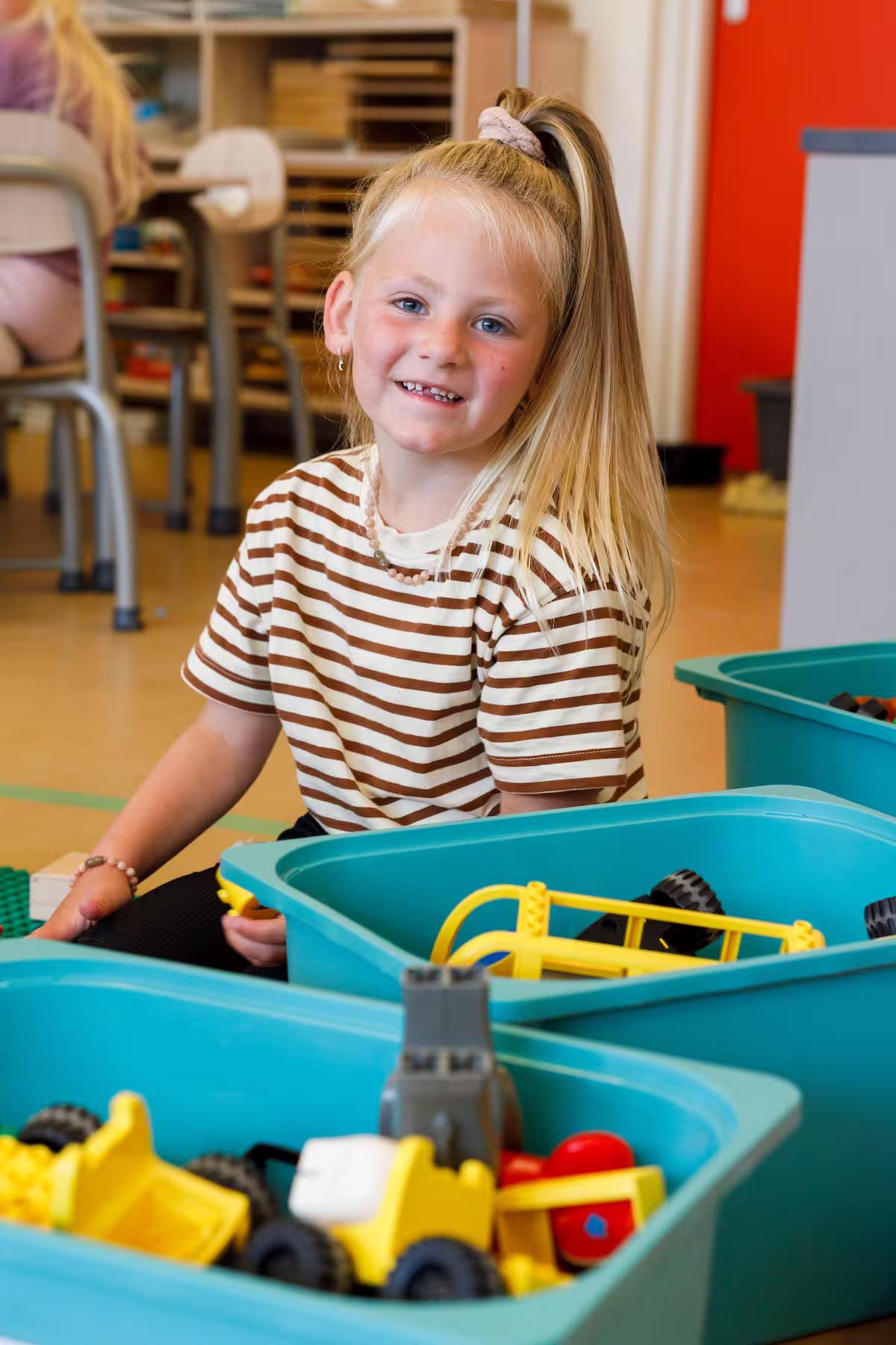 Jong meisje met blond haar en gestreept shirt speelt met bouwspeelgoed in een klaslokaal.