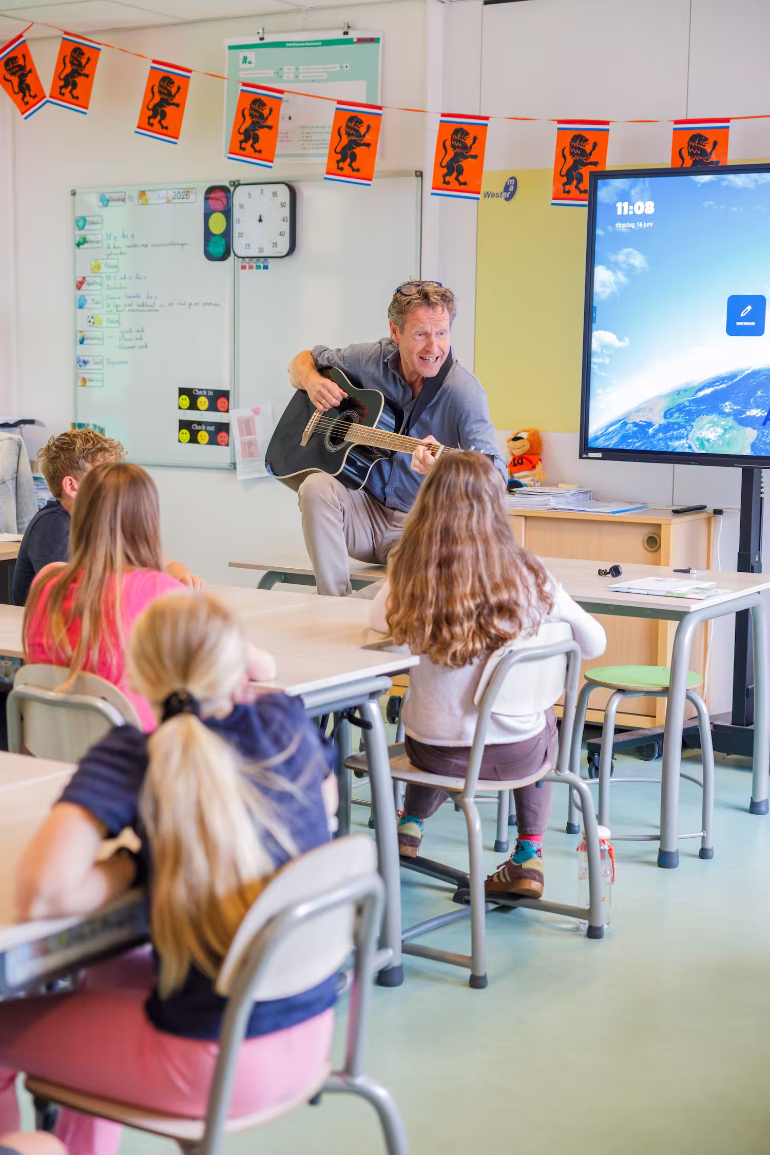 Leraar speelt gitaar voor kinderen die in een klaslokaal op stoelen zitten.