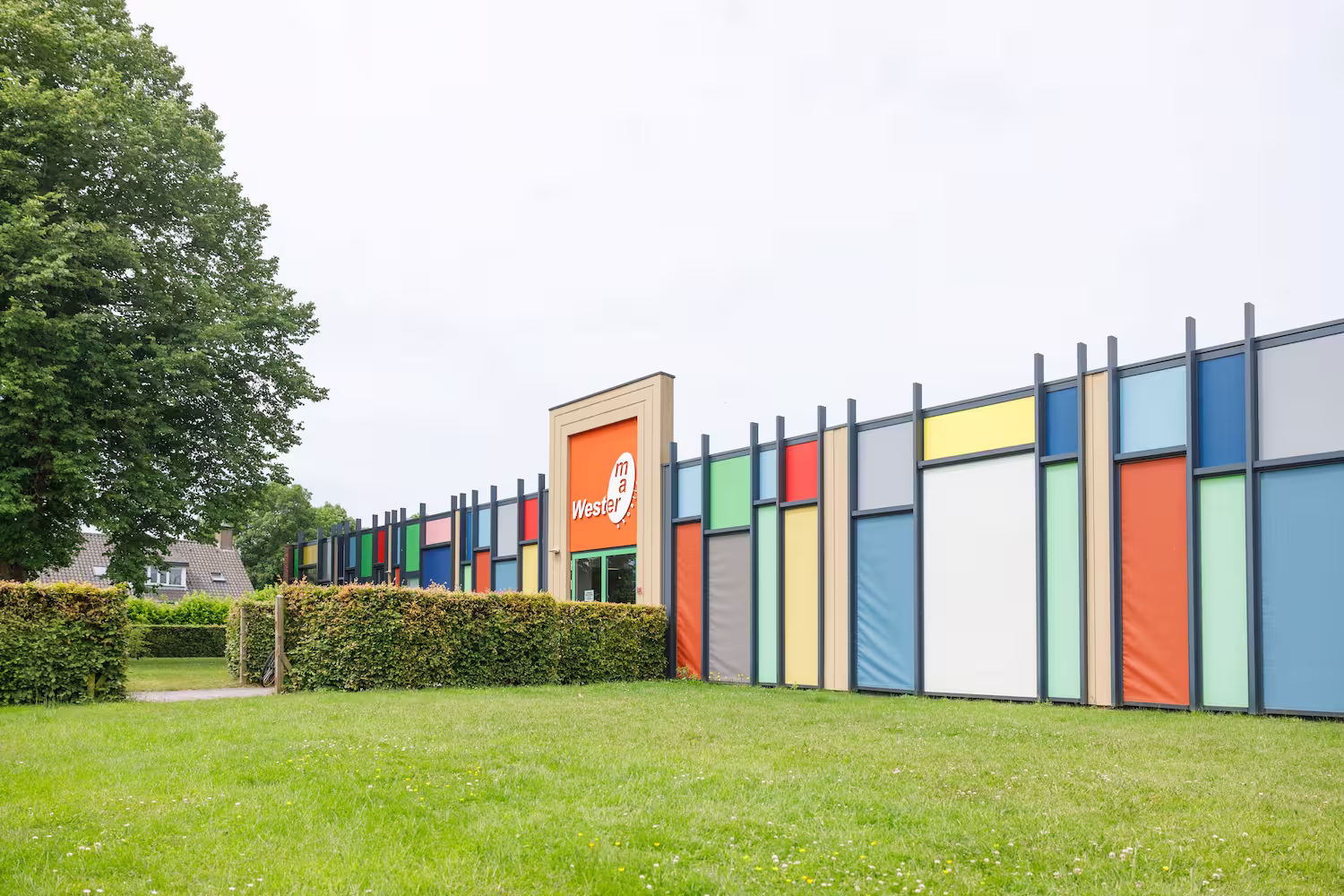 Gebouw met felgekleurde panelen en groene grasmat op de voorgrond.