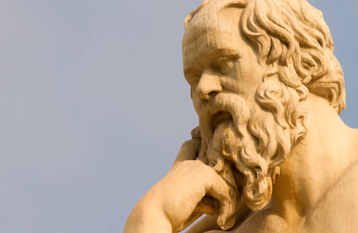Close-up of a classical stone sculpture of a bearded man resting his chin on his hand.