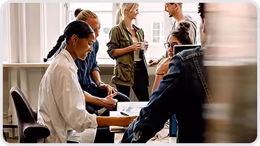 Group of six people having a collaborative discussion around a table in a bright office.