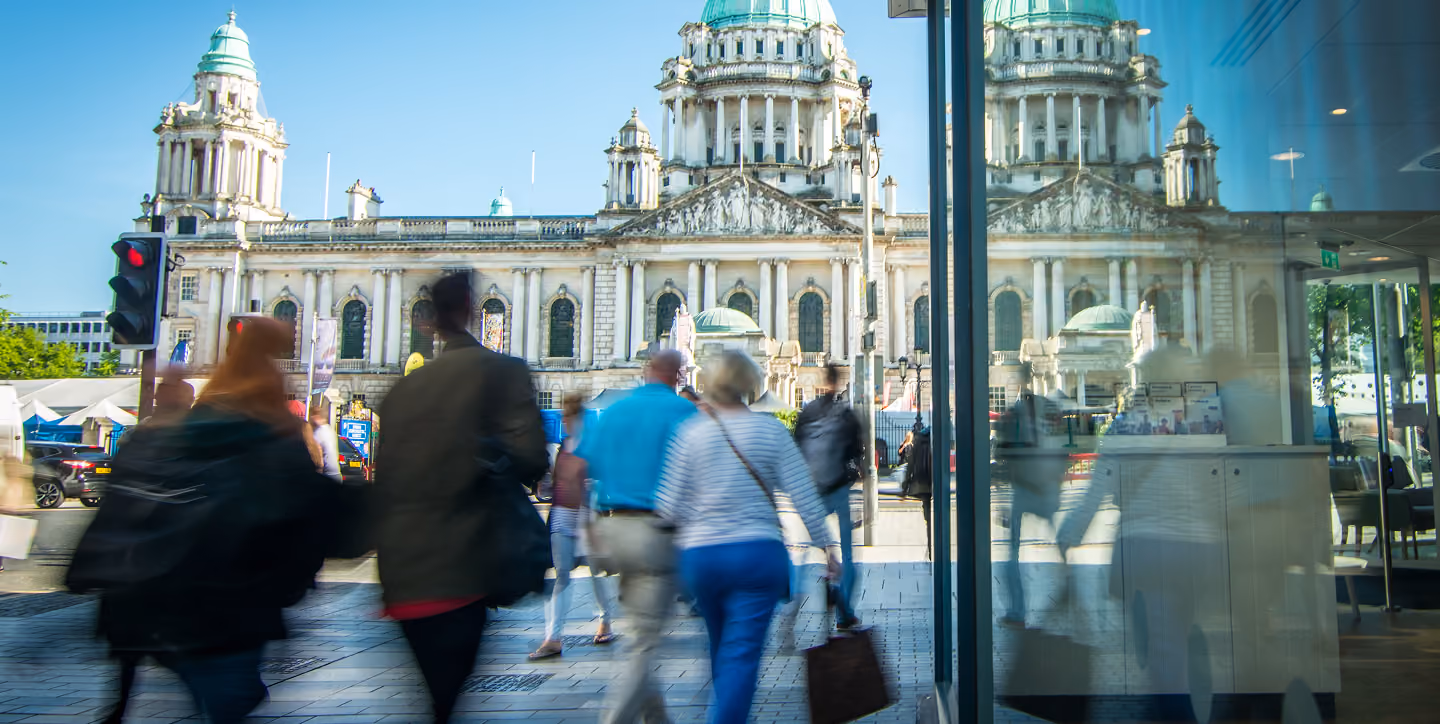 People walking in front of a historic building with domes and columns on a sunny day.