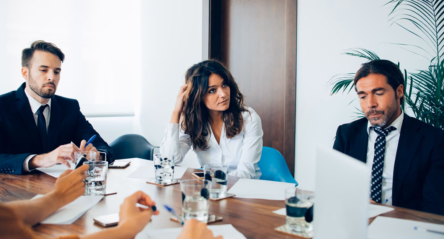 Three business professionals seated at a table with papers and glasses of water during a meeting.