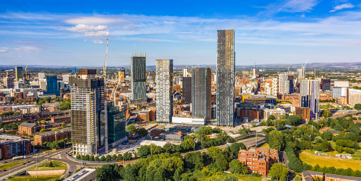 Urban cityscape with modern high-rise buildings, construction cranes, and green parks under a blue sky.
