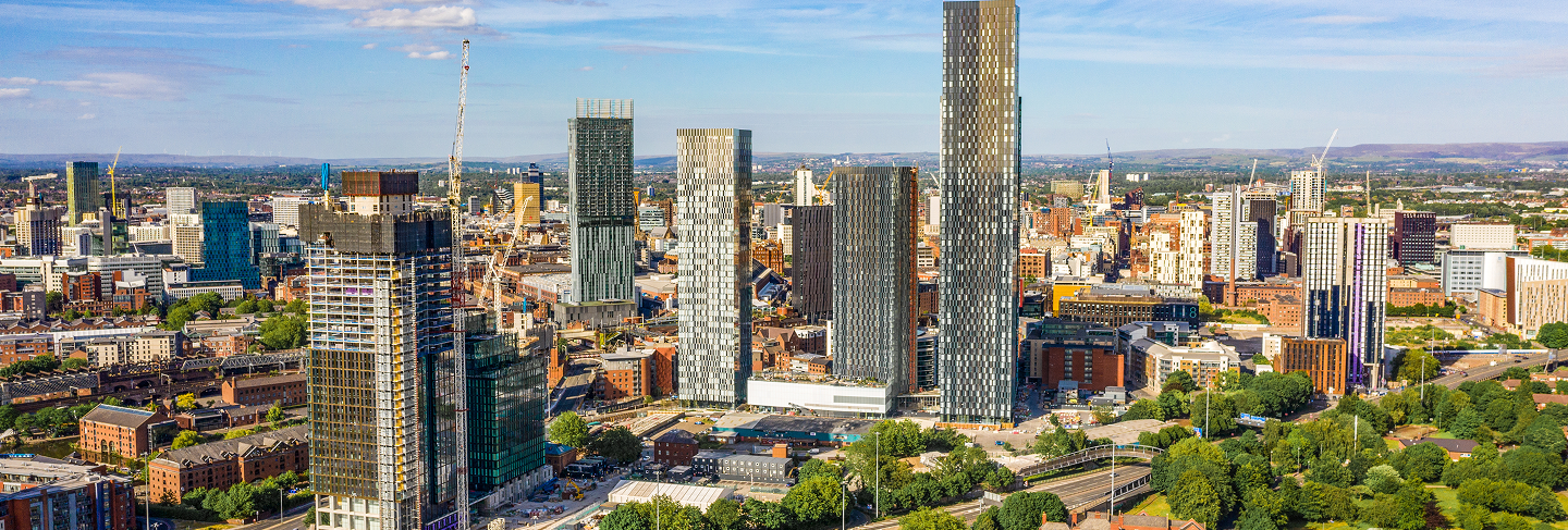 A city skyline with multiple high-rise buildings, some under construction, under a partly cloudy sky.