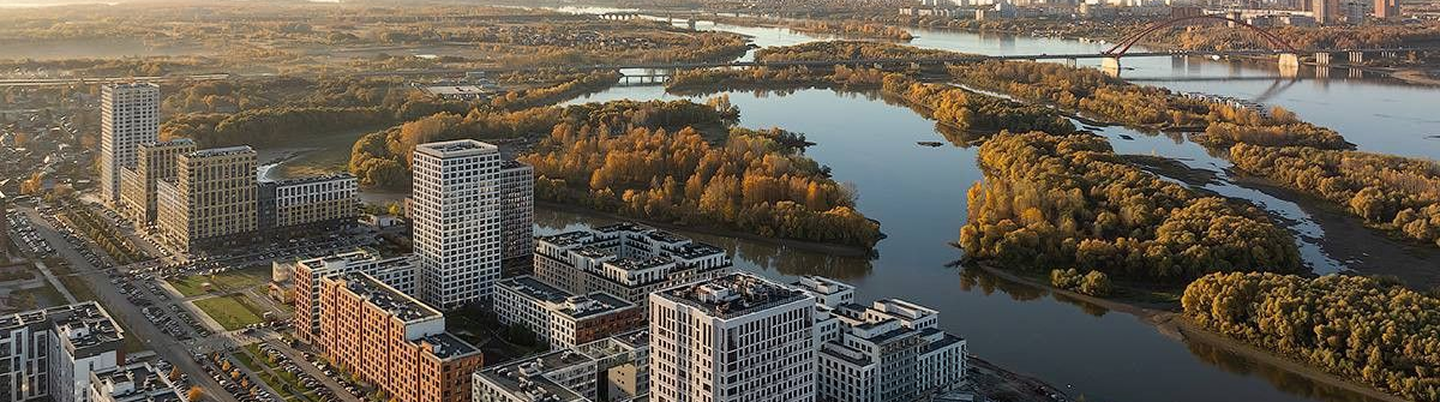 Aerial view of city buildings near a river with tree-covered islands and bridges in a golden hour light.