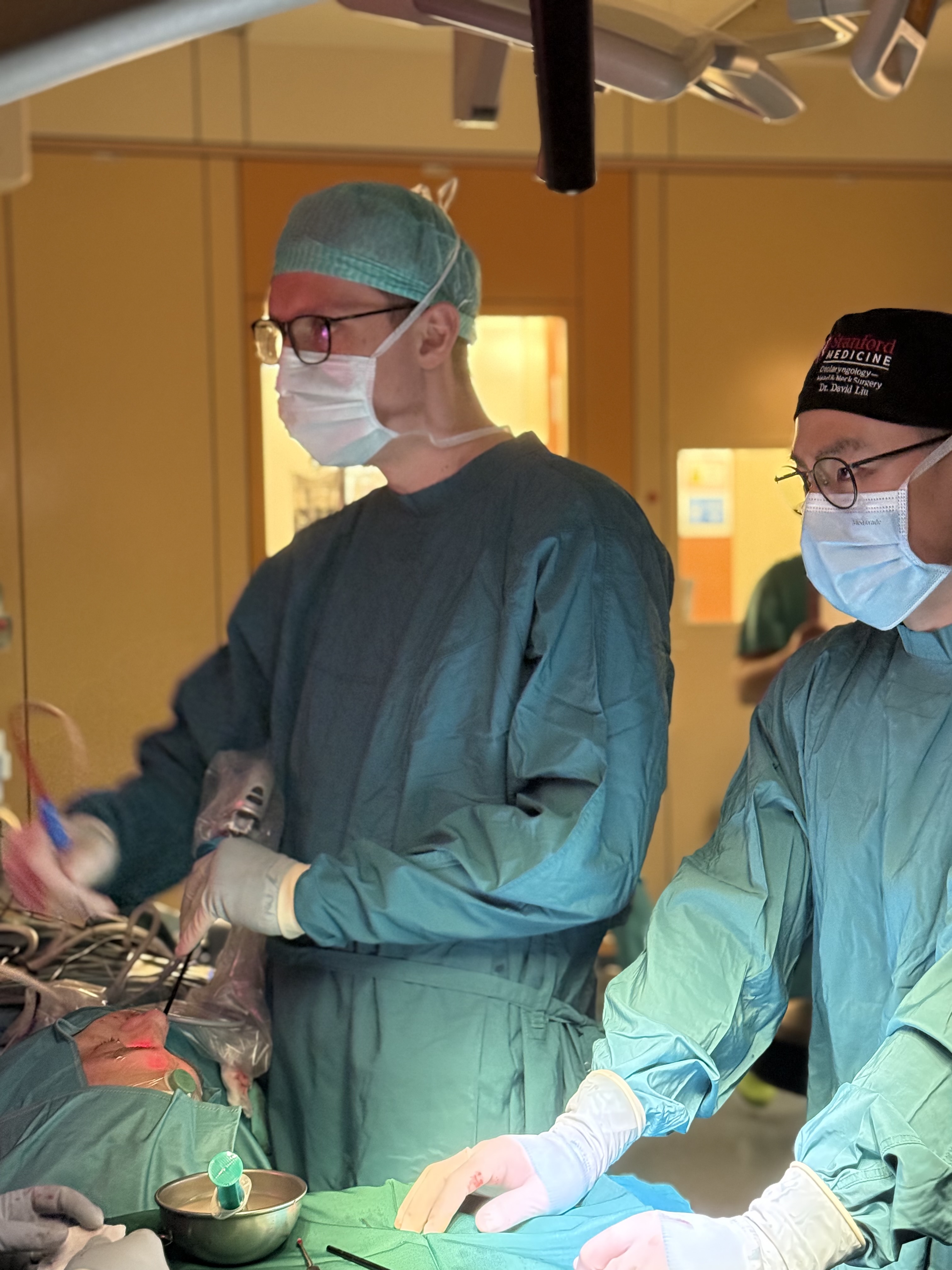 Surgeons in green scrubs performing an operation in the OR, with surgical lights and instruments.