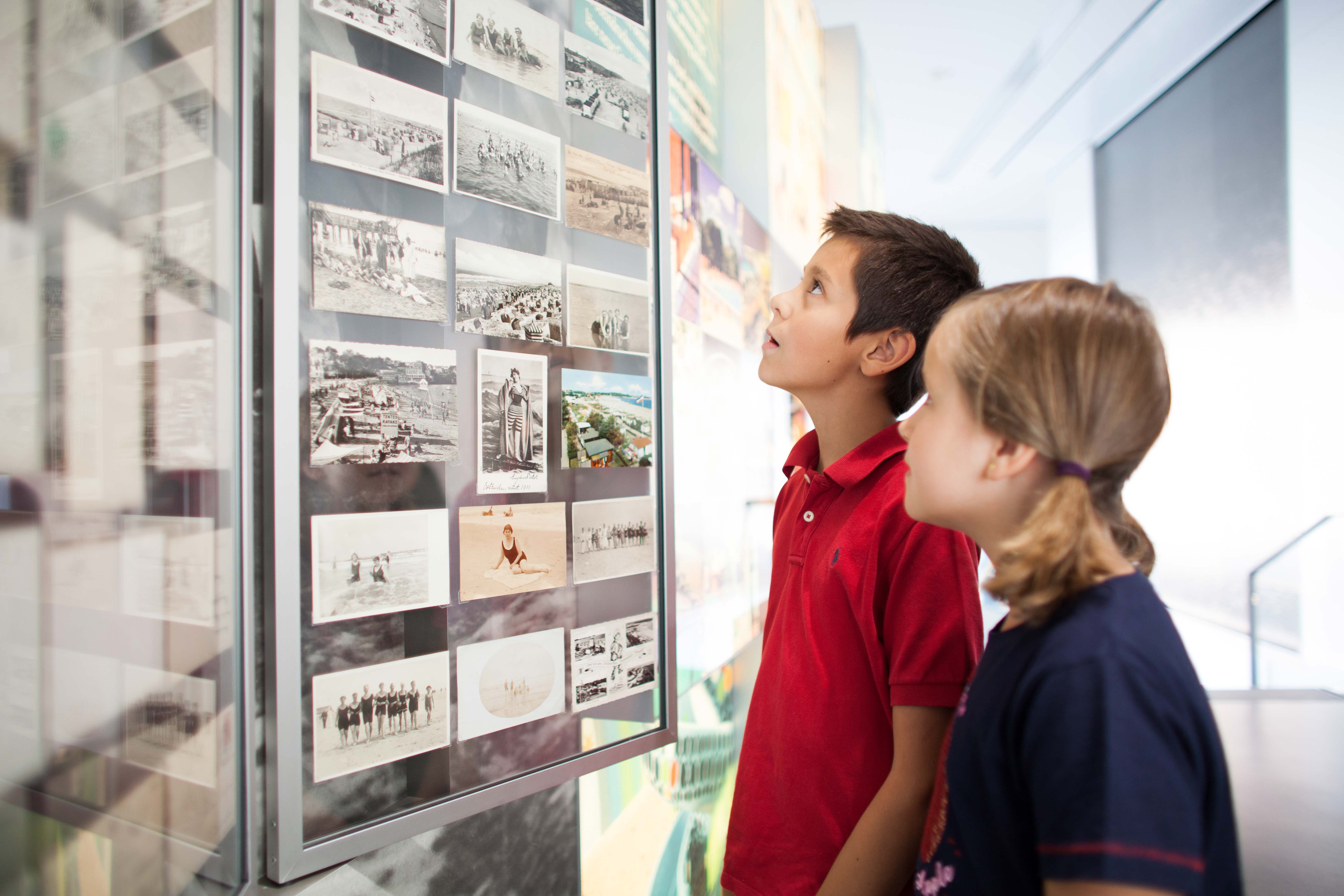 Zwei Kinder betrachten eine Schautafel mit historischen Fotos in der Ausstellung.