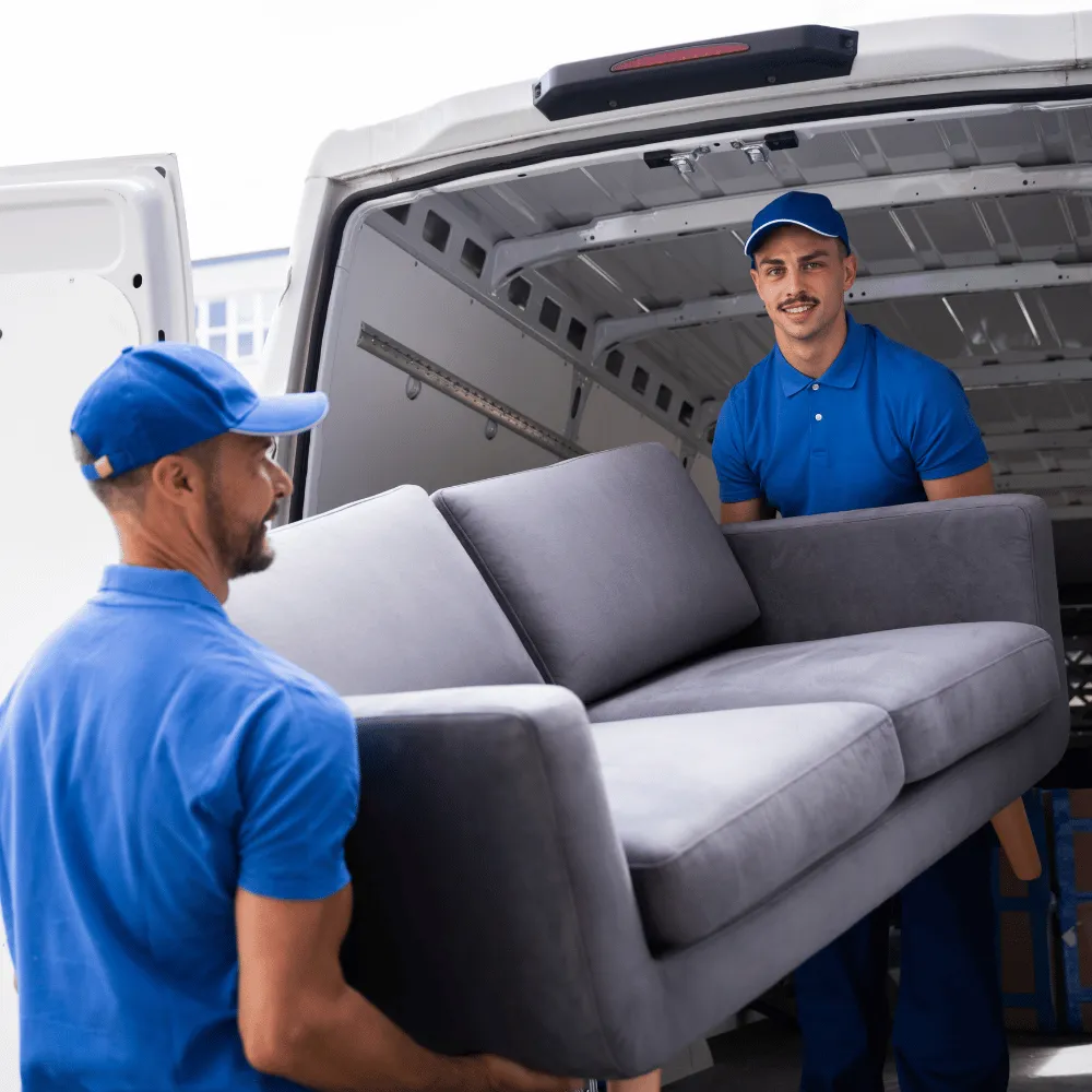 Zwei Umzugshelfer tragen ein graues Sofa zu einem Transporter