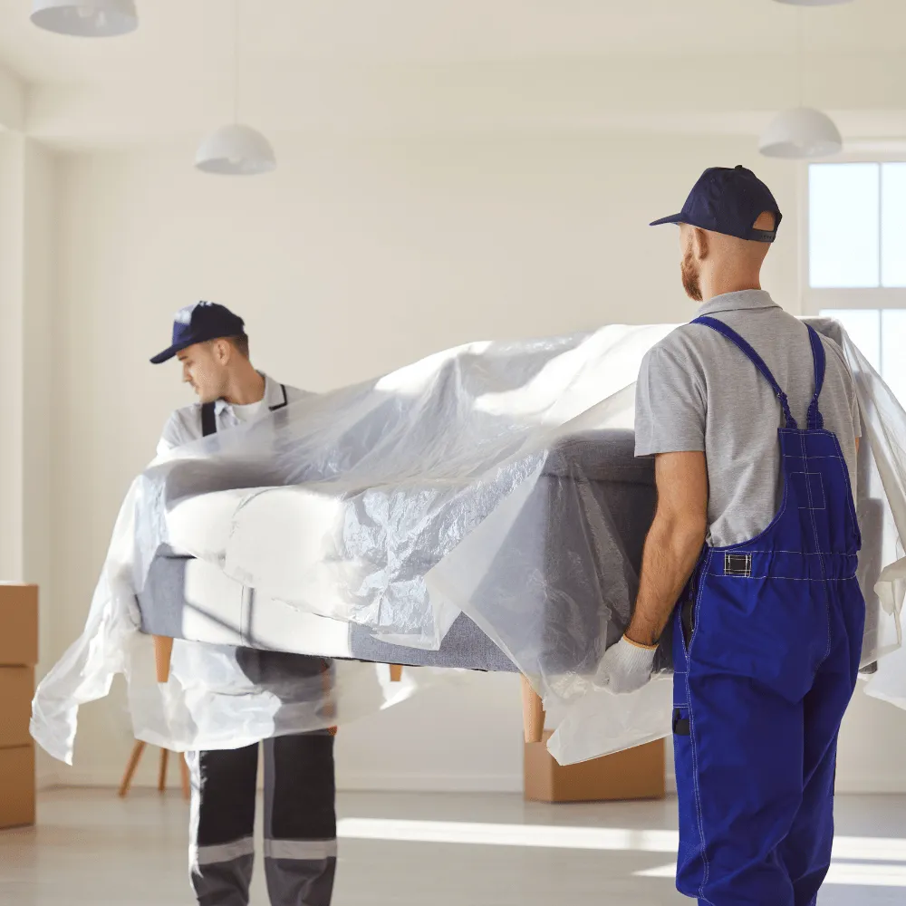 Zwei Umzugshelfer tragen ein geschütztes Sofa durch eine Wohnung