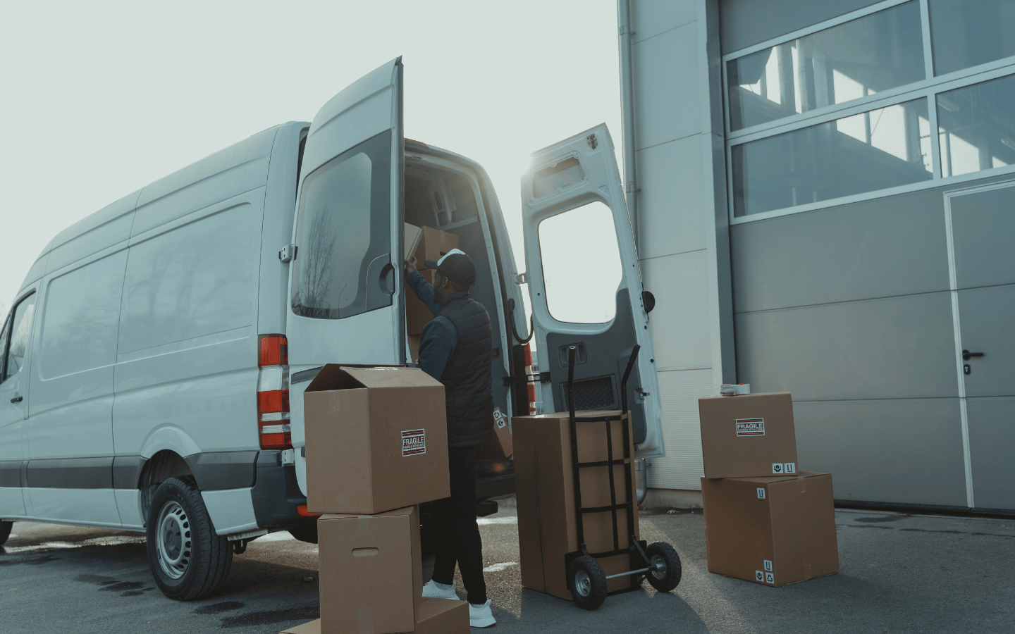 Person lädt Kartons und eine Sackkarre in einen Transporter mit geöffneten Hecktüren vor einer Ladezone