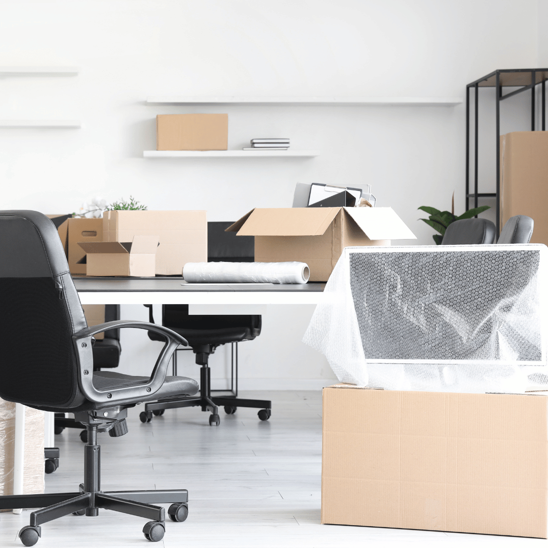 Bürodesk mit Bürostühlen, gepackten Umzugskartons und einem mit Luftpolsterfolie verpackten Monitor