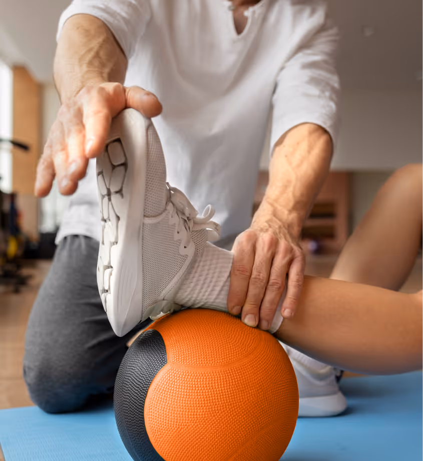 Person stretching leg on an orange and black medicine ball during a workout session.