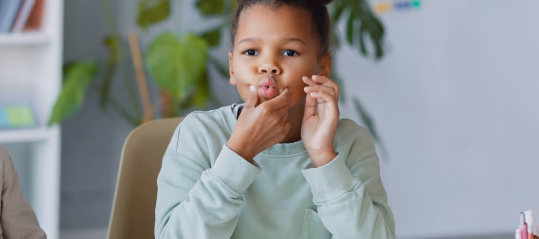Young child practicing speech therapy exercises by puckering lips and touching mouth.