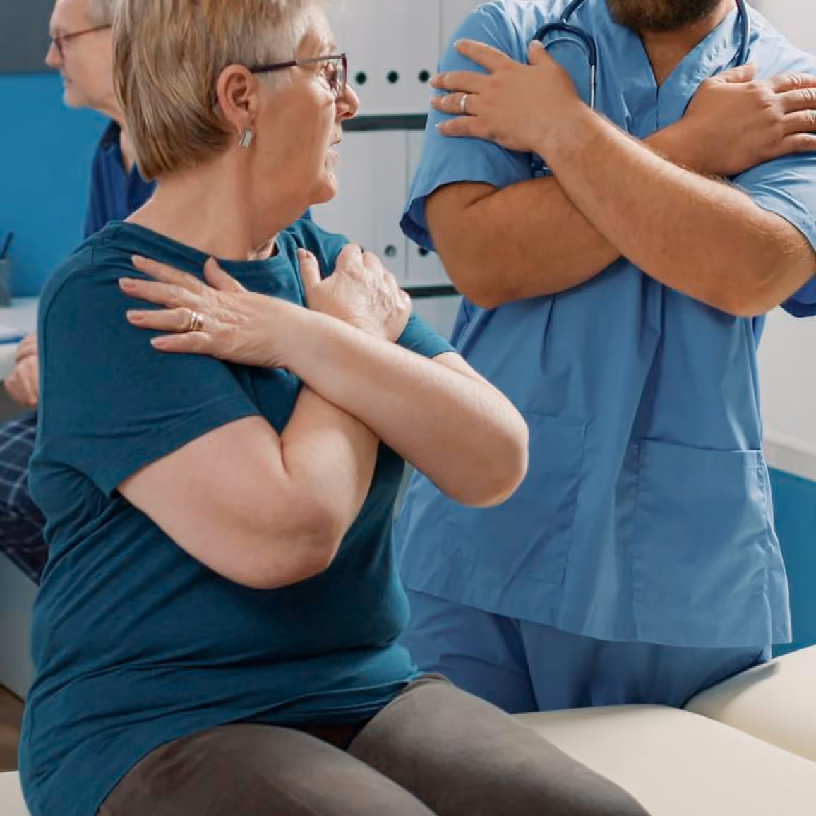 Older woman and male healthcare professional cross arms over shoulders doing seated stretch or exercise.