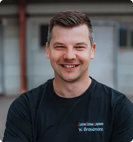Portrait eines lächelnden Mannes mit dunklem T-Shirt vor unscharfem Hintergrund.