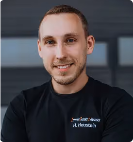 Porträt eines Mannes mit kurzem Haar und Bart, der ein schwarzes T-Shirt mit Firmenlogo trägt.