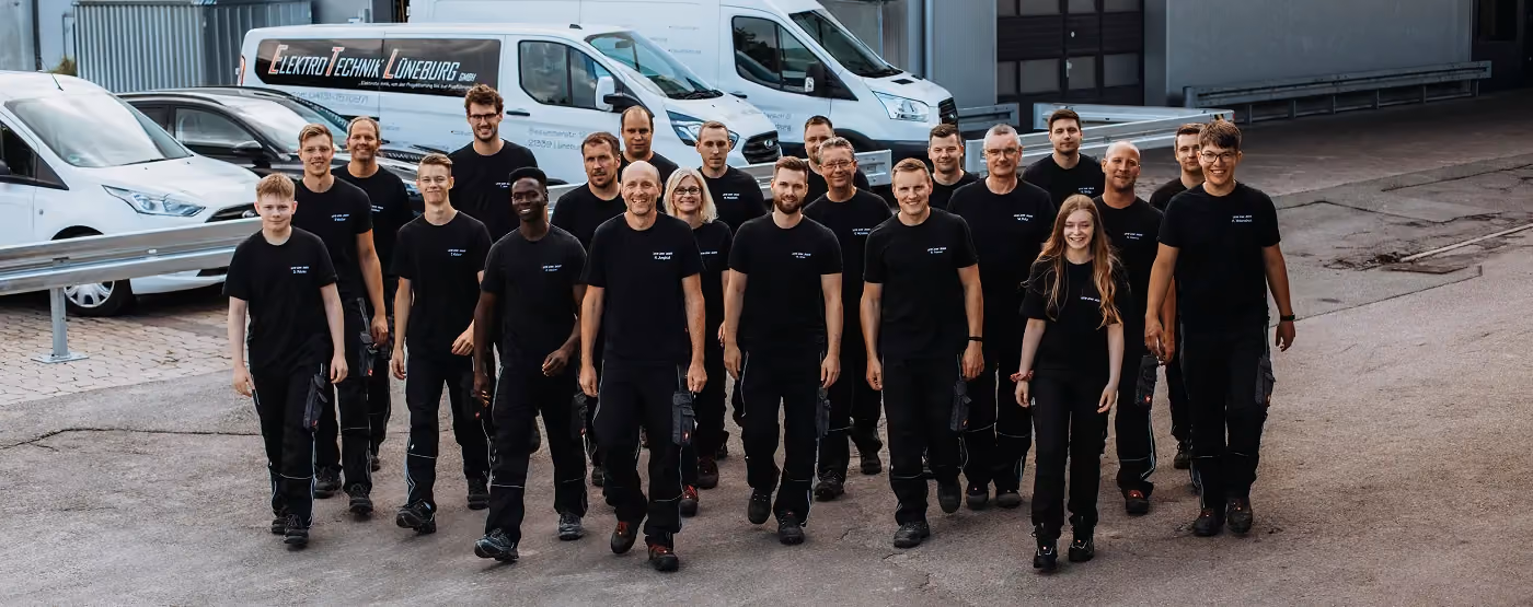 Gruppenbild von 20 Mitarbeitern in schwarzer Arbeitskleidung vor Elektro Technik Lüneburg Vans.