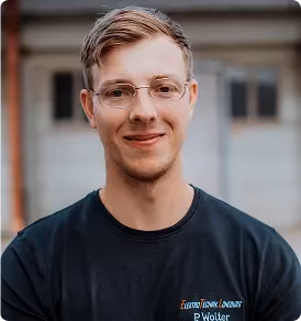 Junger Mann mit Brille und kurzem Haar, lächelnd, trägt schwarzes T-Shirt.