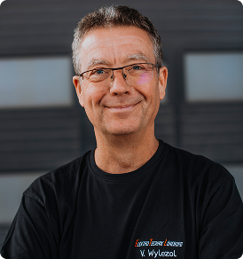 Lächelnder Mann mit Brille und dunklem T-Shirt vor unscharfem Hintergrund.