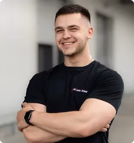 Young man with short hair and beard smiling with arms crossed wearing a black t-shirt and smartwatch.